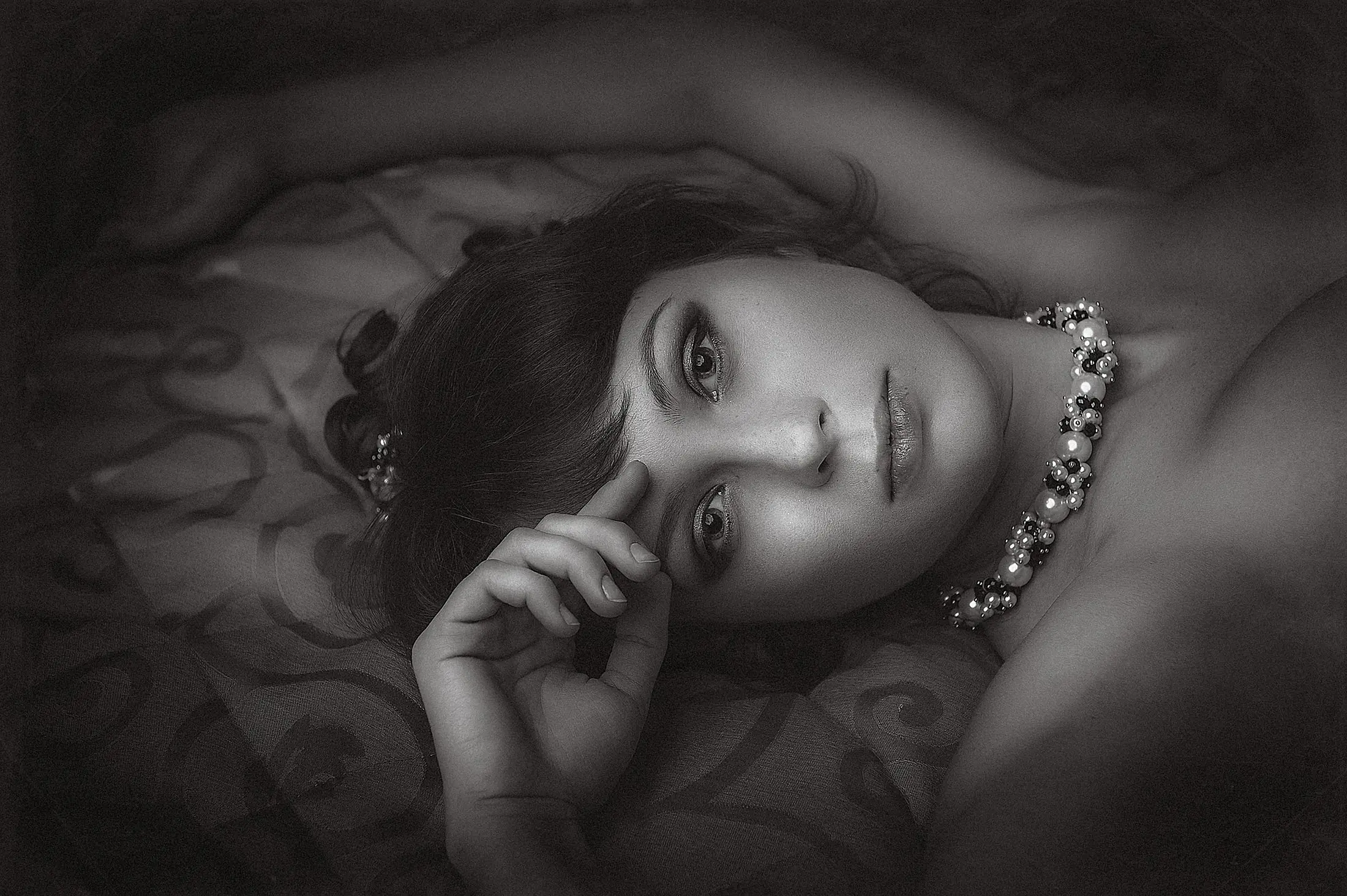 Retrato en blanco y negro de una mujer recostada, con un collar de perlas